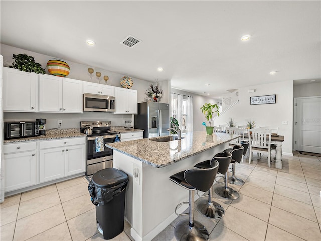 kitchen featuring a center island with sink, white cabinetry, stainless steel appliances, and a breakfast bar area