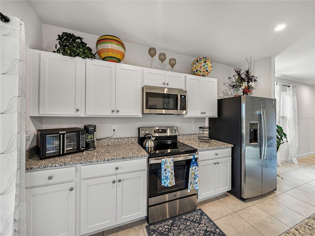 kitchen with light stone countertops, white cabinetry, light tile patterned flooring, and stainless steel appliances