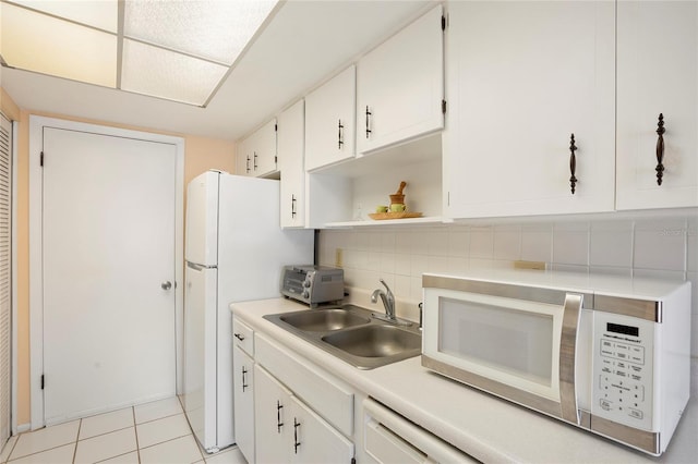 kitchen with white appliances, light tile patterned floors, decorative backsplash, white cabinets, and sink