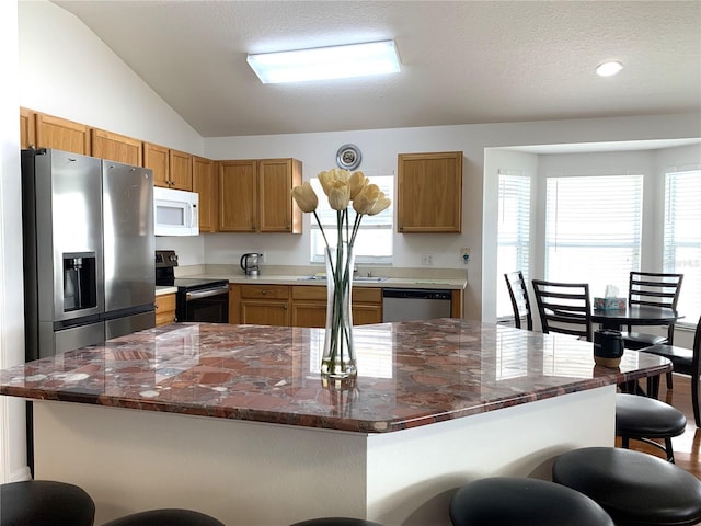 kitchen featuring a wealth of natural light, a center island, stainless steel appliances, vaulted ceiling, and a kitchen bar