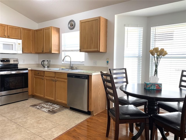 kitchen with appliances with stainless steel finishes, light tile patterned floors, lofted ceiling, and sink