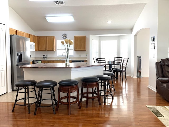 kitchen with a kitchen bar, vaulted ceiling, hardwood / wood-style flooring, stainless steel fridge with ice dispenser, and a center island