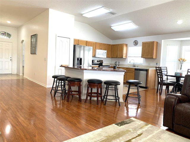 kitchen with appliances with stainless steel finishes, dark hardwood / wood-style flooring, a kitchen breakfast bar, vaulted ceiling, and sink