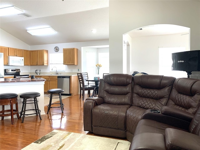 living room with light hardwood / wood-style flooring, vaulted ceiling, and sink