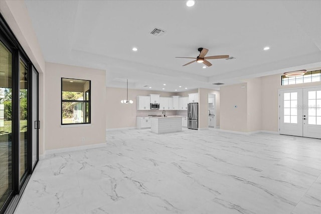 unfurnished living room featuring a raised ceiling, ceiling fan, french doors, and a healthy amount of sunlight