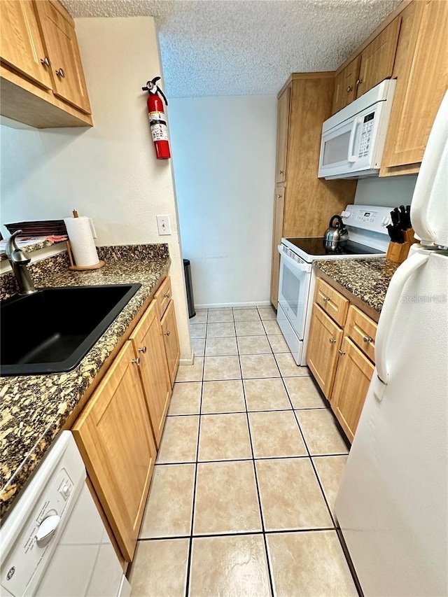 kitchen with sink, a textured ceiling, dark stone countertops, light tile patterned floors, and white appliances