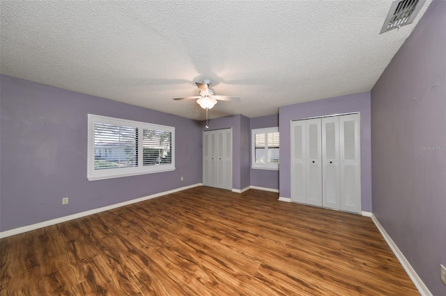 unfurnished bedroom with wood-type flooring, a textured ceiling, two closets, and ceiling fan