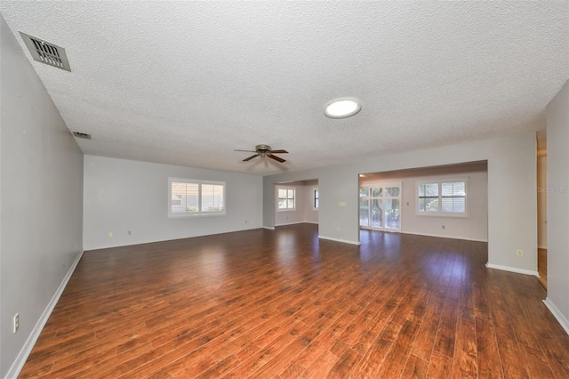 unfurnished living room with a textured ceiling, ceiling fan, dark wood-type flooring, and a wealth of natural light