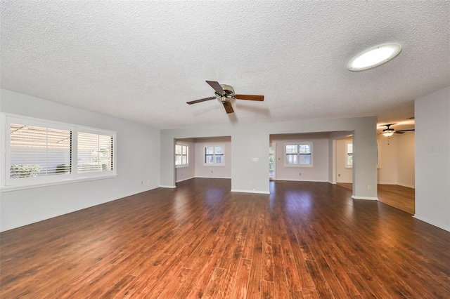 unfurnished living room featuring ceiling fan, a healthy amount of sunlight, dark hardwood / wood-style floors, and a textured ceiling