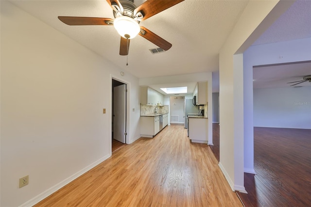 unfurnished living room with sink, a skylight, light hardwood / wood-style flooring, ceiling fan, and a textured ceiling