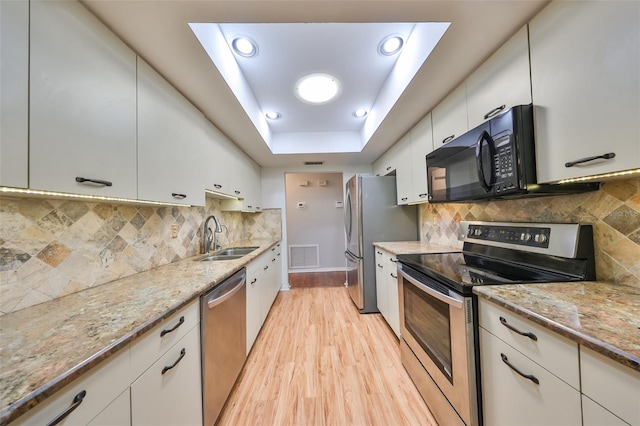 kitchen with sink, stainless steel appliances, light stone counters, light hardwood / wood-style flooring, and white cabinets