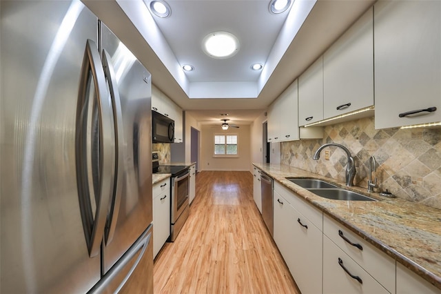 kitchen featuring white cabinetry, sink, light stone countertops, stainless steel appliances, and a raised ceiling