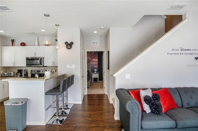 kitchen with white cabinetry, hanging light fixtures, stainless steel appliances, dark hardwood / wood-style flooring, and a breakfast bar