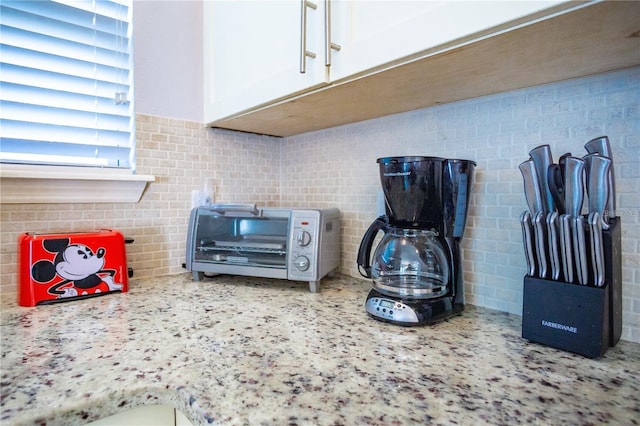 room details featuring white cabinets, backsplash, and light stone counters