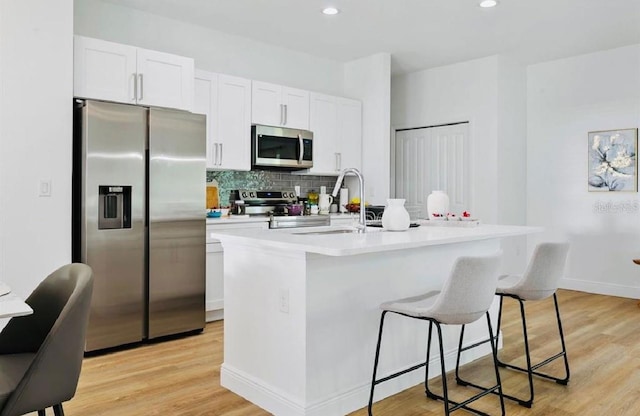 kitchen featuring white cabinetry, a center island with sink, stainless steel appliances, and light wood-type flooring