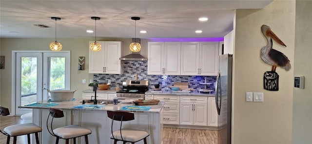 kitchen with tasteful backsplash, wall chimney exhaust hood, stainless steel appliances, white cabinetry, and hanging light fixtures