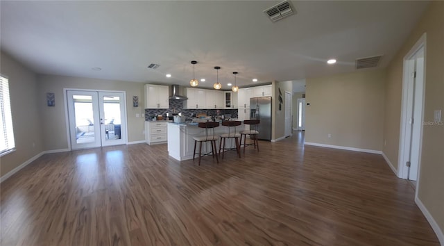 kitchen featuring stainless steel refrigerator with ice dispenser, a kitchen island, wall chimney range hood, pendant lighting, and white cabinetry