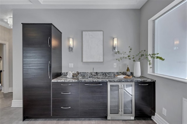 interior space featuring sink, beverage cooler, light stone counters, dark brown cabinets, and ornamental molding