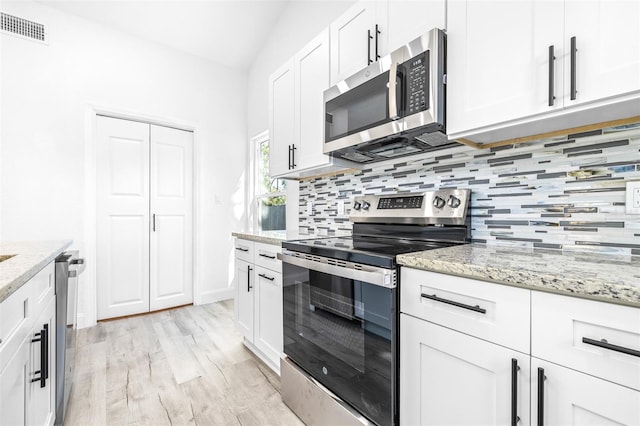 kitchen featuring decorative backsplash, light stone counters, stainless steel appliances, white cabinets, and light hardwood / wood-style floors