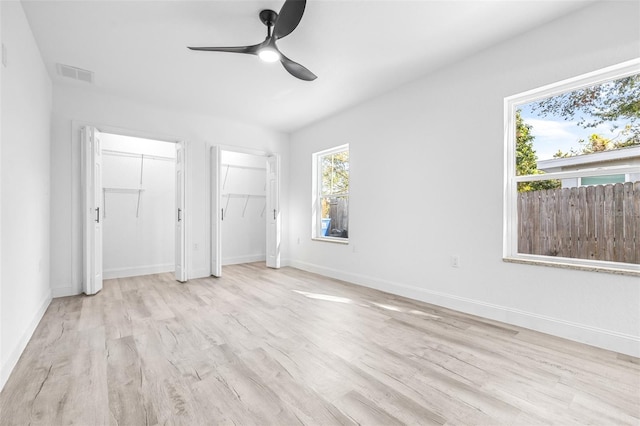 unfurnished bedroom with ceiling fan, light hardwood / wood-style floors, and two closets