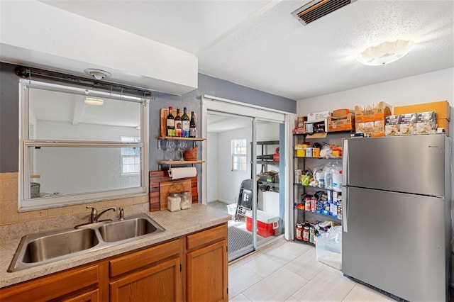 kitchen with a textured ceiling, stainless steel fridge, and sink