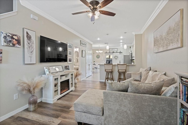 living room with ceiling fan with notable chandelier, crown molding, and dark wood-type flooring