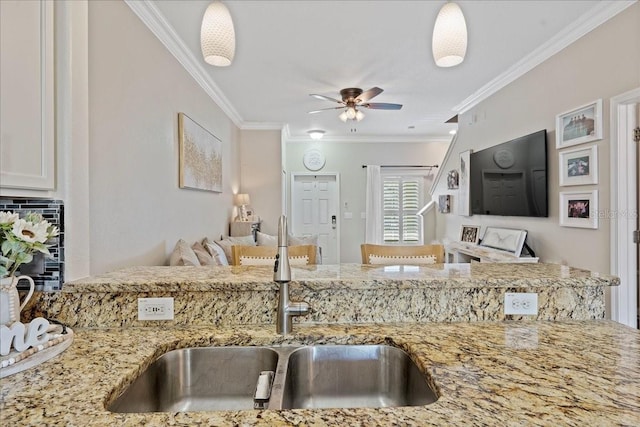 kitchen featuring pendant lighting, light stone counters, crown molding, and sink