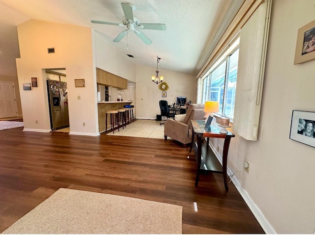 living room featuring ceiling fan with notable chandelier, wood-type flooring, a textured ceiling, and vaulted ceiling