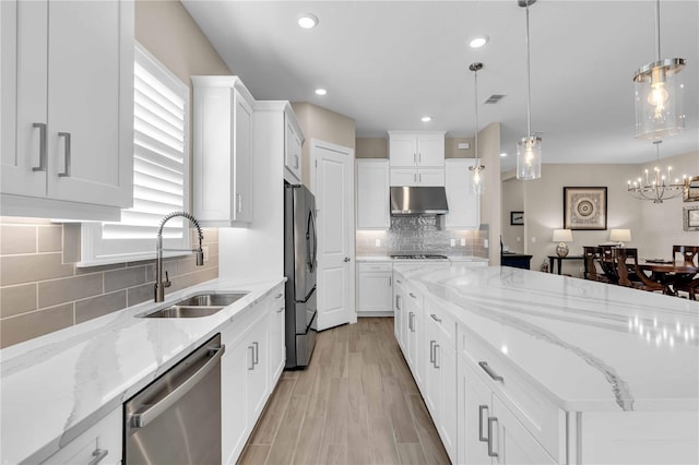 kitchen with light stone counters, stainless steel appliances, sink, pendant lighting, and white cabinetry