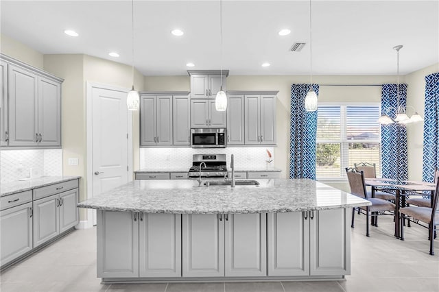 kitchen featuring gray cabinetry, hanging light fixtures, an island with sink, and stainless steel appliances