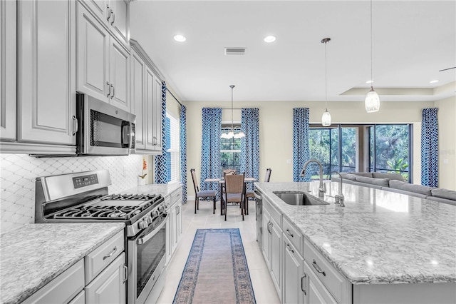 kitchen featuring tasteful backsplash, stainless steel appliances, a kitchen island with sink, sink, and decorative light fixtures