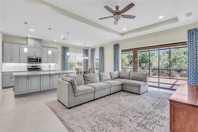 living room with ceiling fan, a raised ceiling, sink, and a wealth of natural light