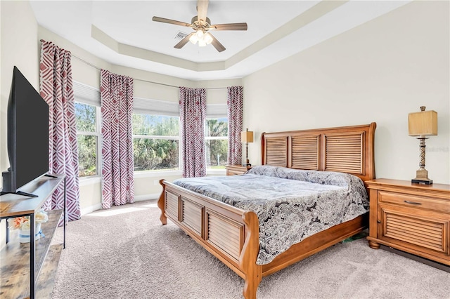 carpeted bedroom featuring a tray ceiling and ceiling fan