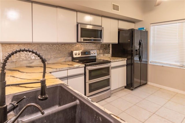 kitchen featuring white cabinets, light tile patterned floors, stainless steel appliances, and light stone counters