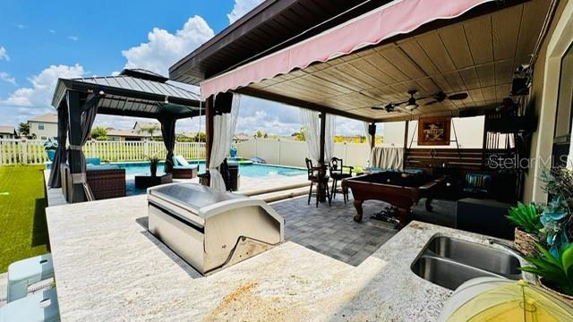 view of patio / terrace featuring an outdoor kitchen, sink, a gazebo, a fenced in pool, and a grill