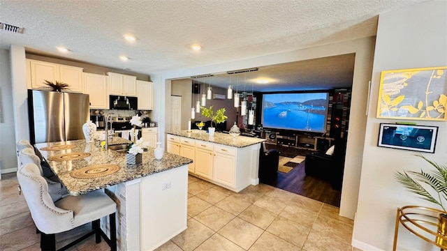 kitchen with a center island with sink, light stone countertops, decorative light fixtures, white cabinetry, and stainless steel appliances