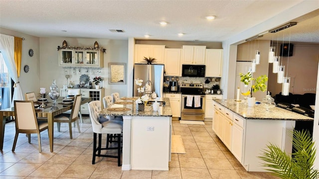 kitchen featuring a center island with sink, light stone countertops, stainless steel appliances, and a textured ceiling