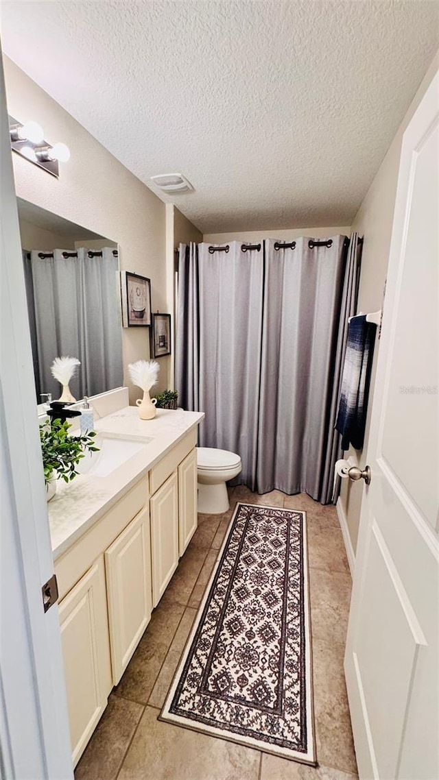 bathroom featuring tile patterned flooring, a textured ceiling, vanity, and toilet