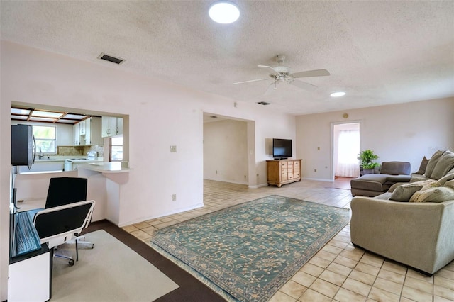 living room with a textured ceiling, a wealth of natural light, ceiling fan, and light tile patterned flooring