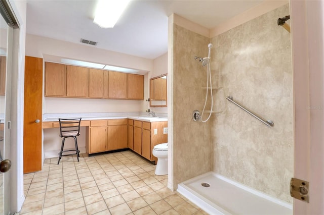 bathroom with a tile shower, vanity, tile patterned floors, and toilet