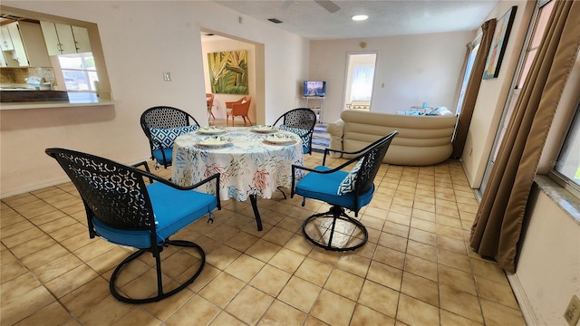 dining area with ceiling fan, light tile patterned floors, a textured ceiling, and baseboards