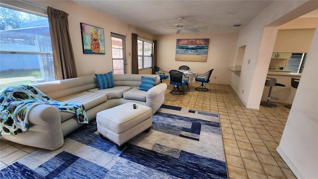 living room featuring light tile patterned floors, visible vents, baseboards, a ceiling fan, and a textured ceiling