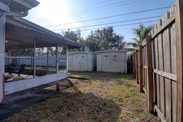 view of yard featuring a sunroom, a fenced backyard, a storage unit, and an outbuilding