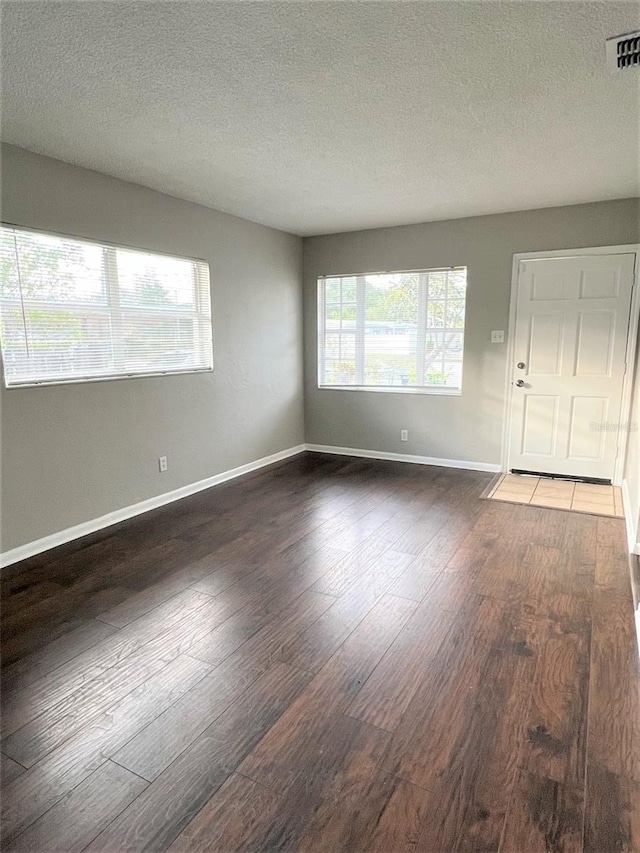 spare room featuring a textured ceiling, dark hardwood / wood-style floors, and a wealth of natural light