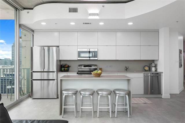 kitchen featuring white cabinetry, a wall of windows, stainless steel appliances, and a breakfast bar