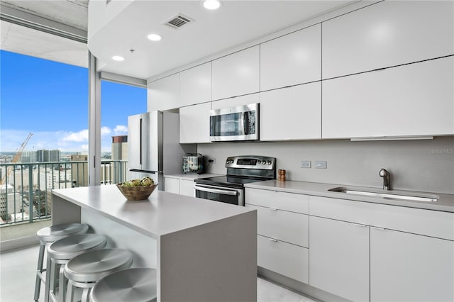 kitchen featuring sink, a breakfast bar area, white cabinetry, appliances with stainless steel finishes, and a kitchen island