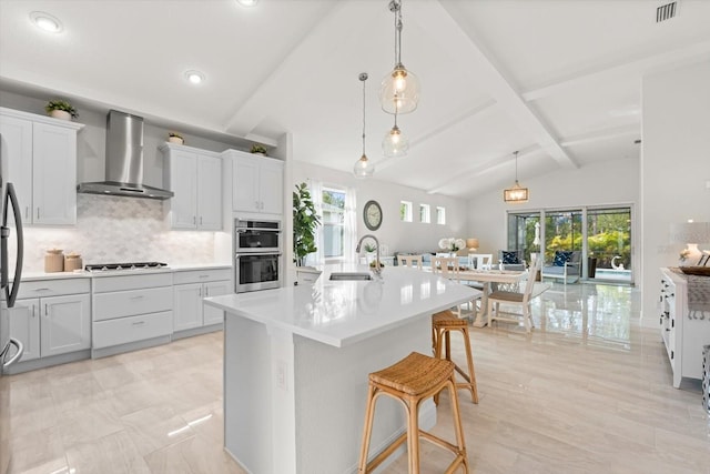 kitchen featuring vaulted ceiling with beams, stainless steel appliances, visible vents, a sink, and wall chimney exhaust hood