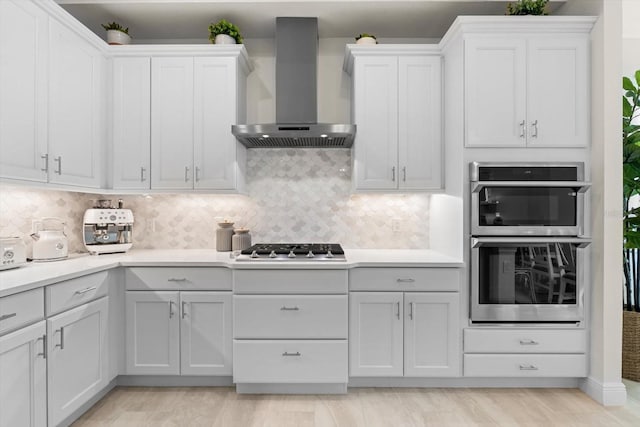 kitchen featuring tasteful backsplash, white cabinets, wall chimney exhaust hood, and appliances with stainless steel finishes