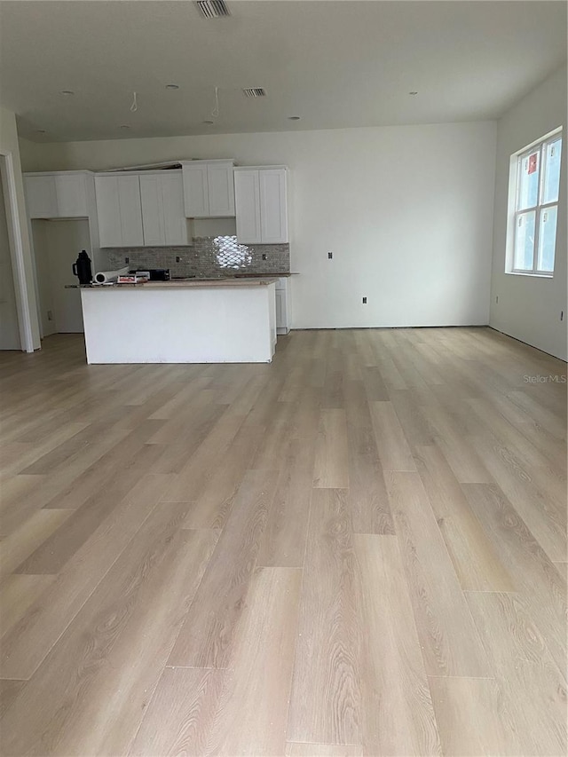 kitchen featuring light wood-type flooring, white cabinets, tasteful backsplash, and a center island