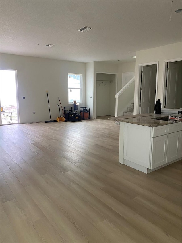 kitchen with sink, white cabinetry, dark stone counters, and light wood-type flooring